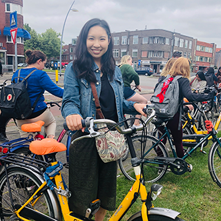 Young woman stands next to a bicycle with her hands on the handlebars.