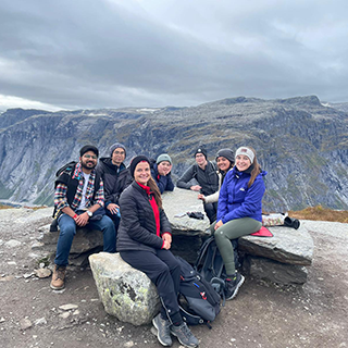 A group of college students sit on a rock formation near Trolltunga.