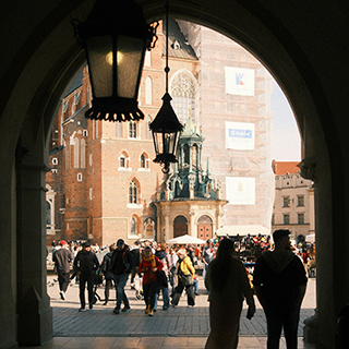 View through and archway with metal hanging lanterns with view of historic buildings beyond.