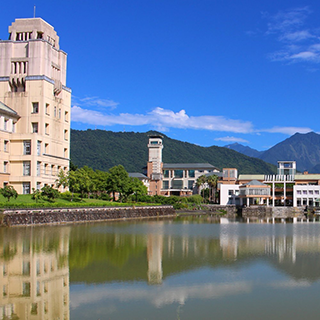 Buildings line a lake with mountains and blue sky in the background.