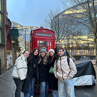 College students in winter coats pose in front of a red British telephone booth.