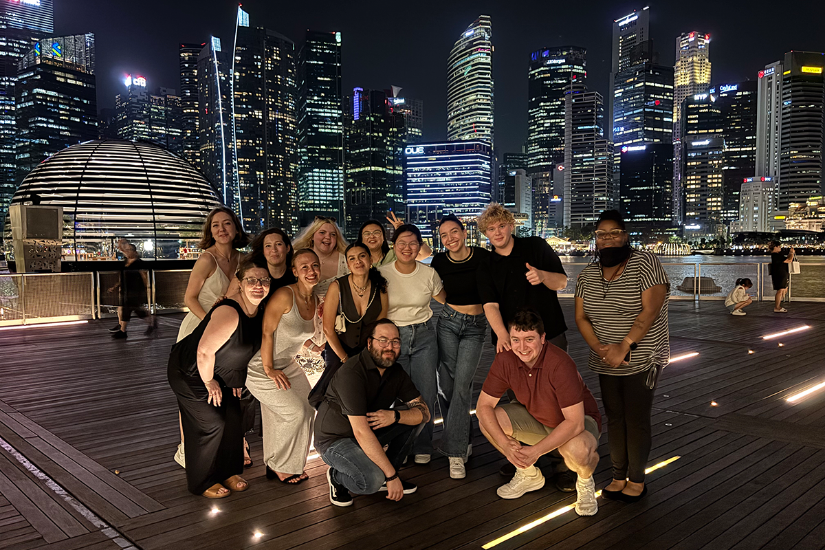 Group of college students pose together in Singapore with the city skyline behind them at night.
