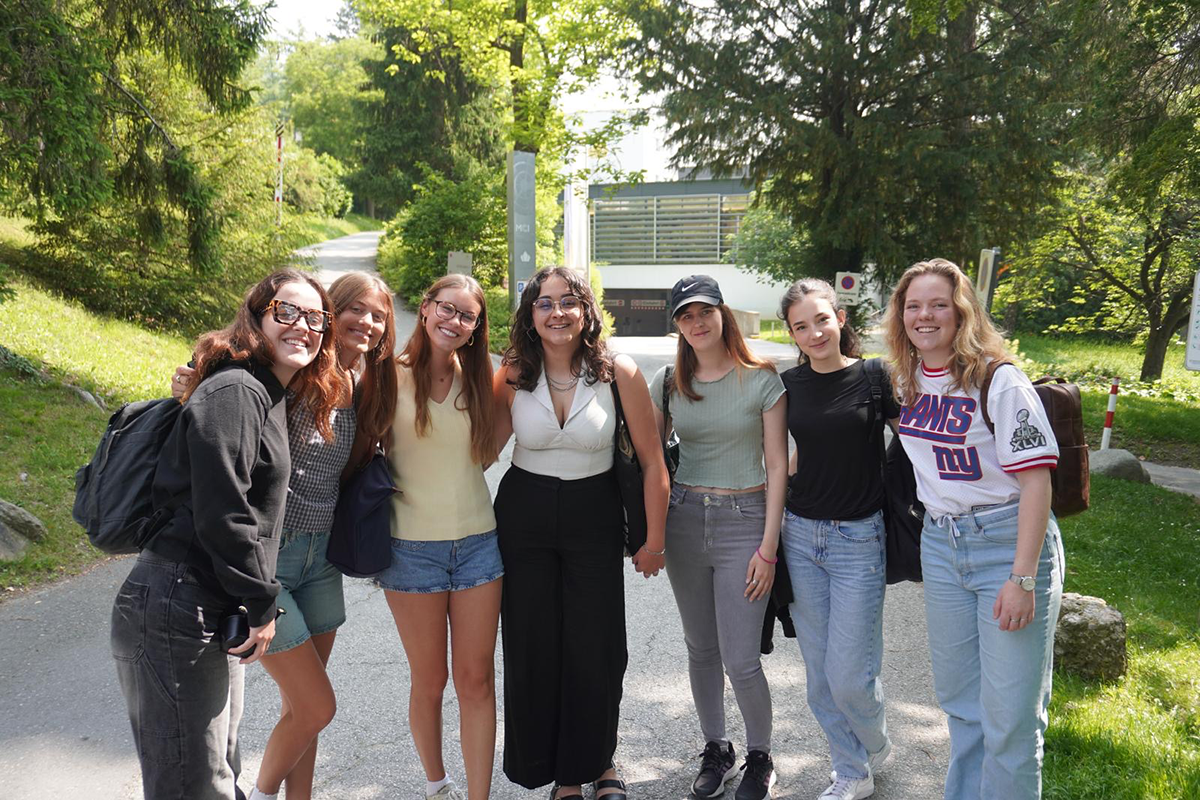 Seven college students pose for a photo outside surrounded by greenery.