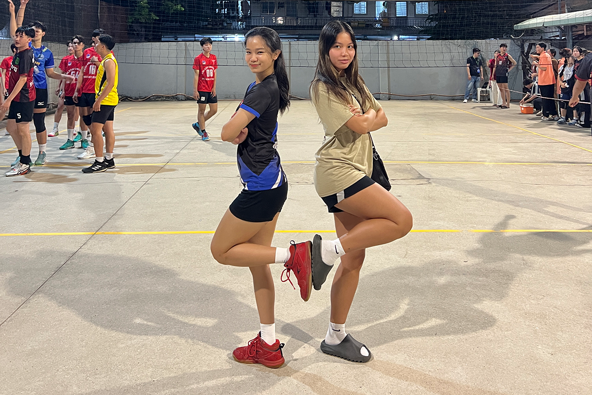 two young woman stand back to back on an athletic court.