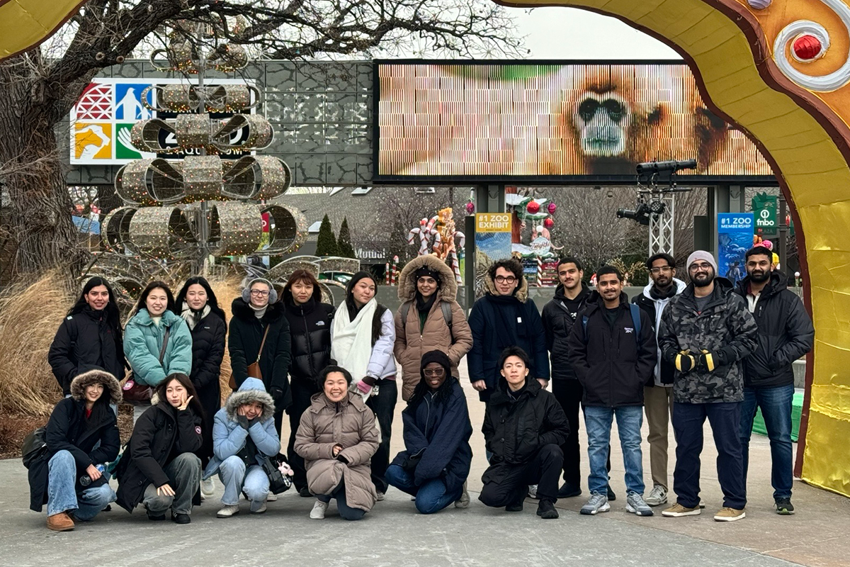 Group of college students pose in front of a zoo entrance gates in cold weather.