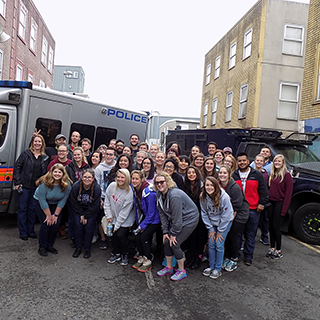 Group of college students poses in front of a UK police van.