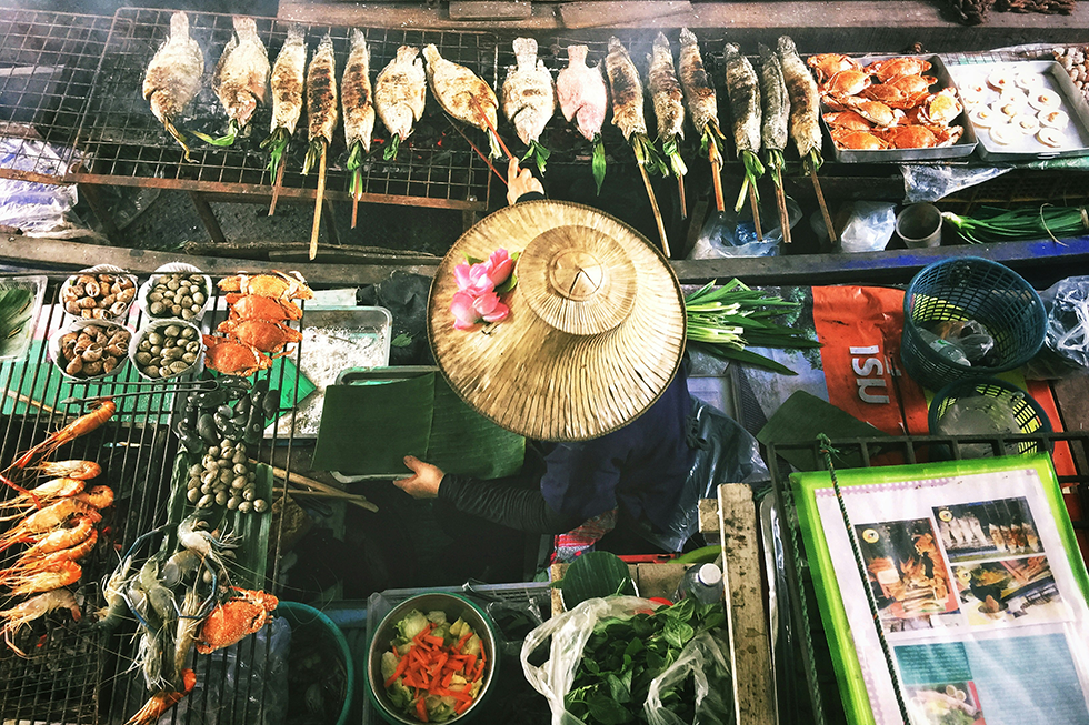 View from above of a woman wearing a straw hat, cooking fish and other food.