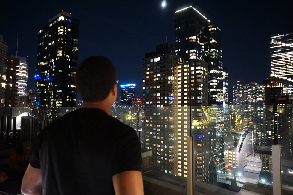 Young man looks out over a city skyline at night.