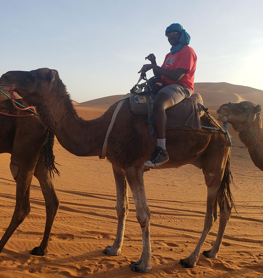 A UNO student sits a top a camel in the deserts of Morocco