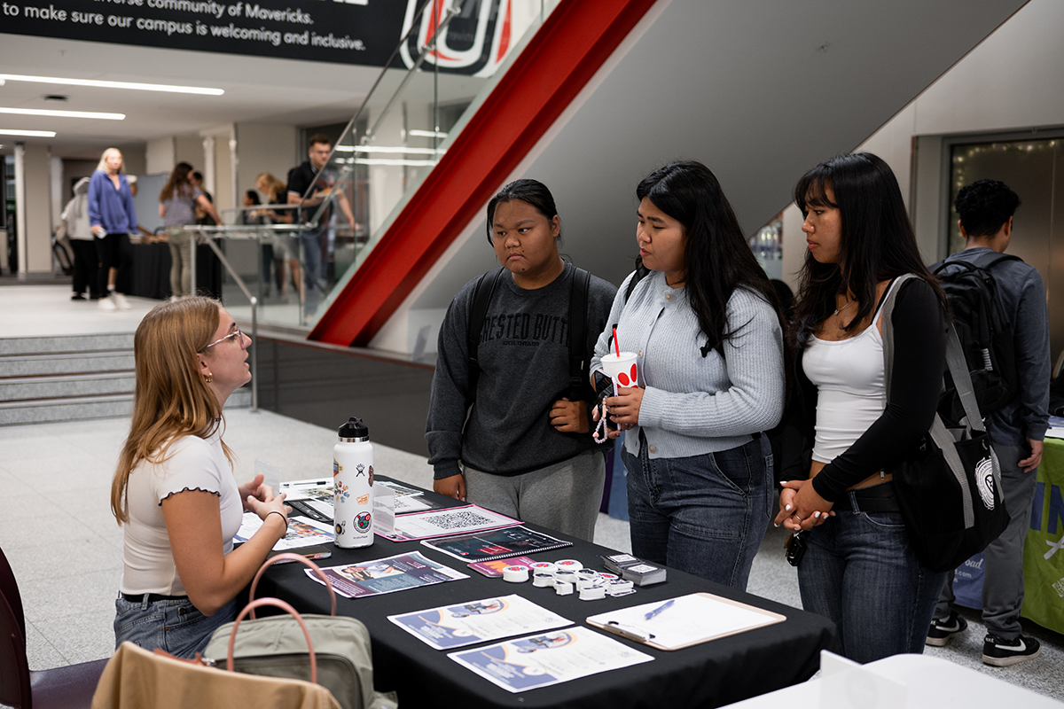 A woman sitting at a table speaks to three women standing in front of the table.