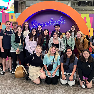 Group of college students pose in front of a neon business sign in Brazil.