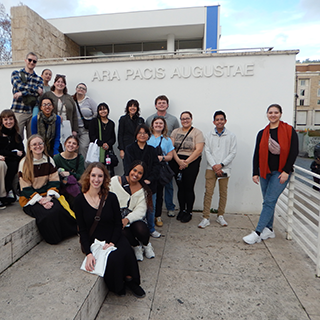 Group of college students pose on the steps outside a white building.