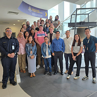 Group poses in front of a staircase and a sign that reads, 'Singapore Prison Service'.