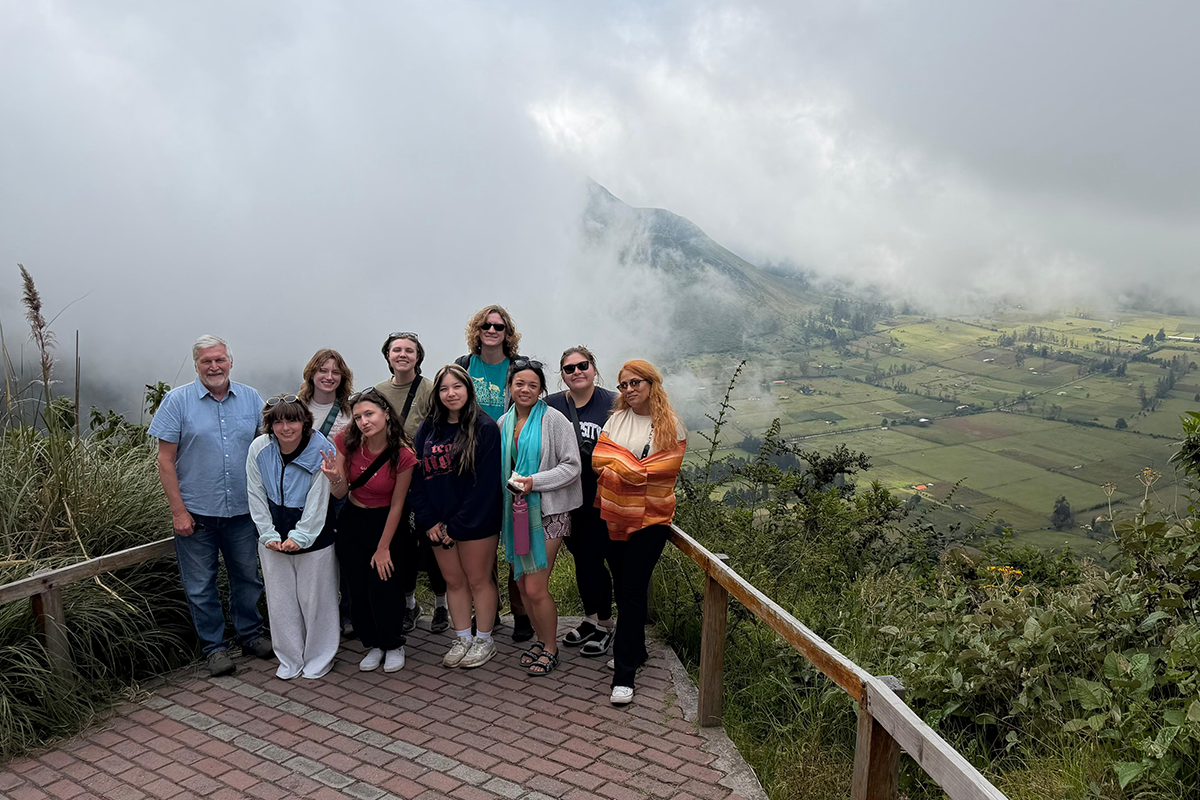 Group of 10 people pose at an overlook with clouds and green fields in the distance.