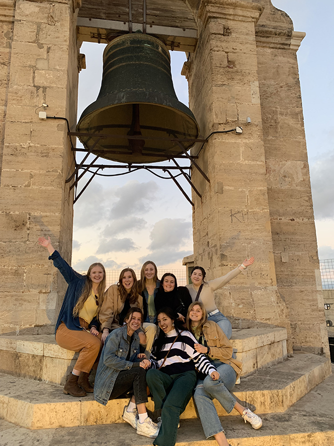 A UNO student and her friends pose underneath a large bell tower in Spain