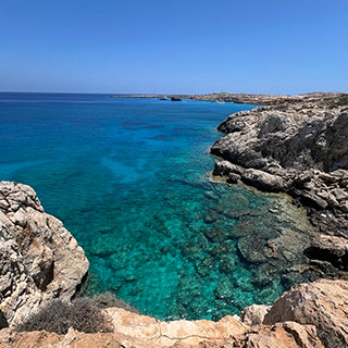 Blue water of the ocean surrounded on three sides by craggy rocks.