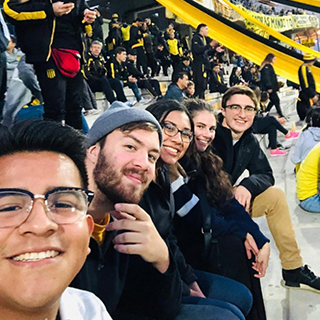 College students sit in a row on a bleacher at a sporting event.