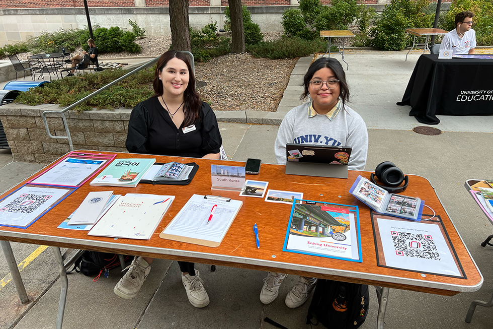 Two students sit at a table outside at the study abroad fair.