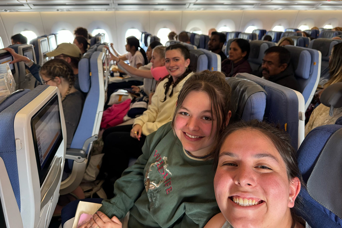 Three young women sitting on an airplane smile for the camera.
