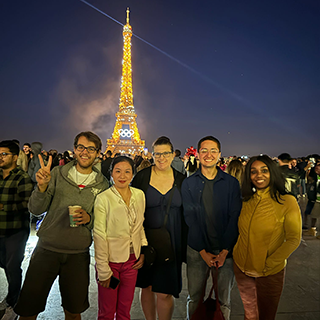 Five college students pose in front of the Eiffel Tower at night.