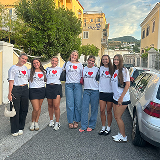 Seven women stand in the street wearing 'I heart Ischia' t-shirts.