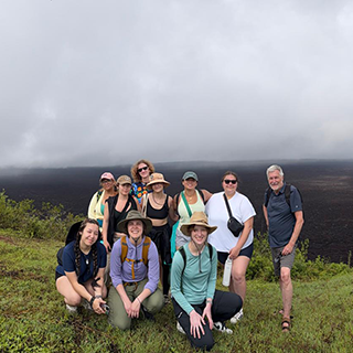 A group poses together on a green hillside with cloudy sky behind.
