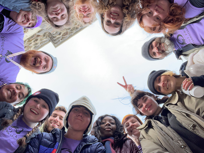 UNO students form a circle and look down at the camera for a group picture