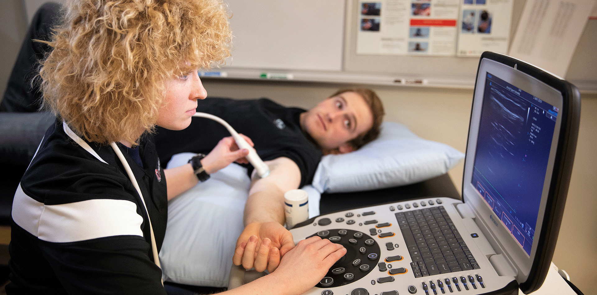 a young woman performs an ultrasound on a young man's arm.