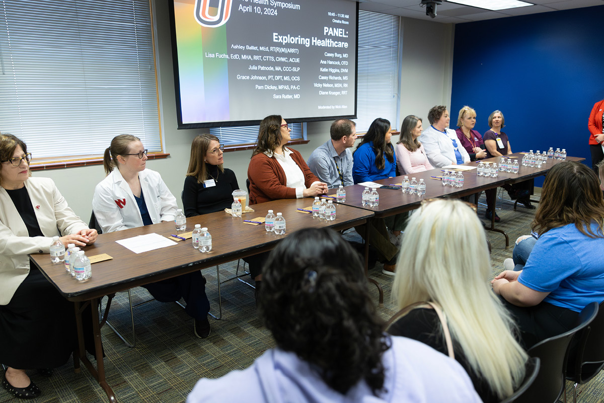 A long table of panelists of varying medical professions sit together at a conference. 