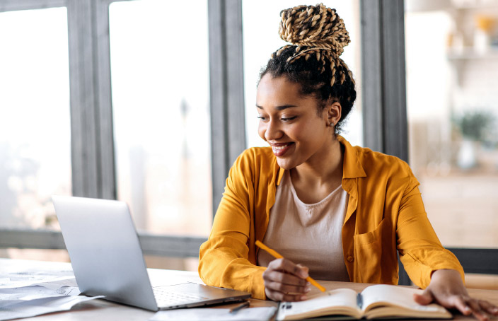 Student using a laptop and taking notes at a desk.