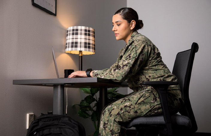 Person in military uniform using a laptop at a desk.