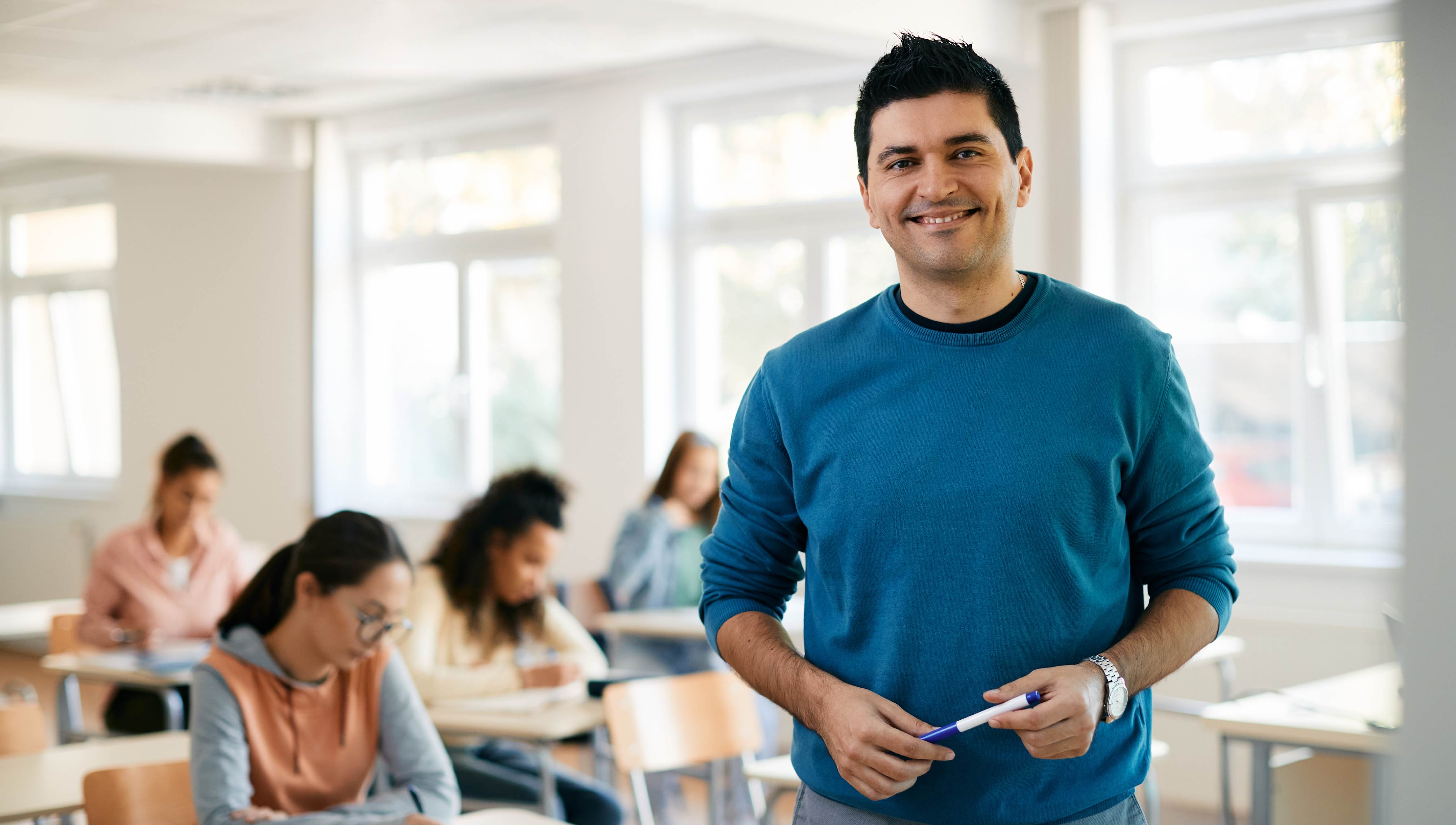 Teacher standing at the front of a classroom while students work independently.
