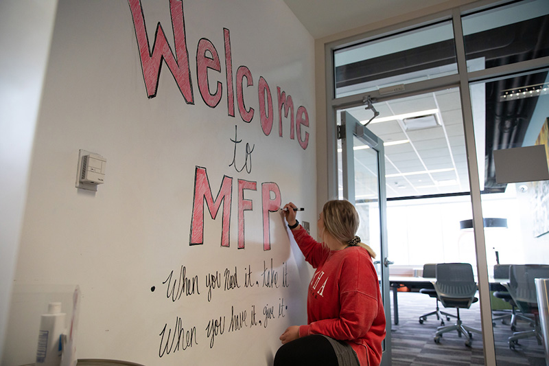 student making a "Welcome to the Maverick Food Pantry" sign on the dry-erase wall