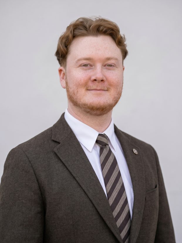 Head-and-shoulders portrait of a person in a dark suit and striped tie against a plain light background.