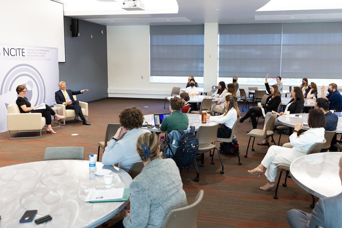 This photo shows people seated at tables and chairs listening to DHS Deputy Secretary John Tien, who is engaging with the audience.