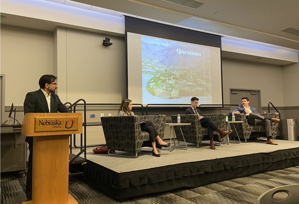 Moderator stands at a podium to the left of stage with seated panelists. 