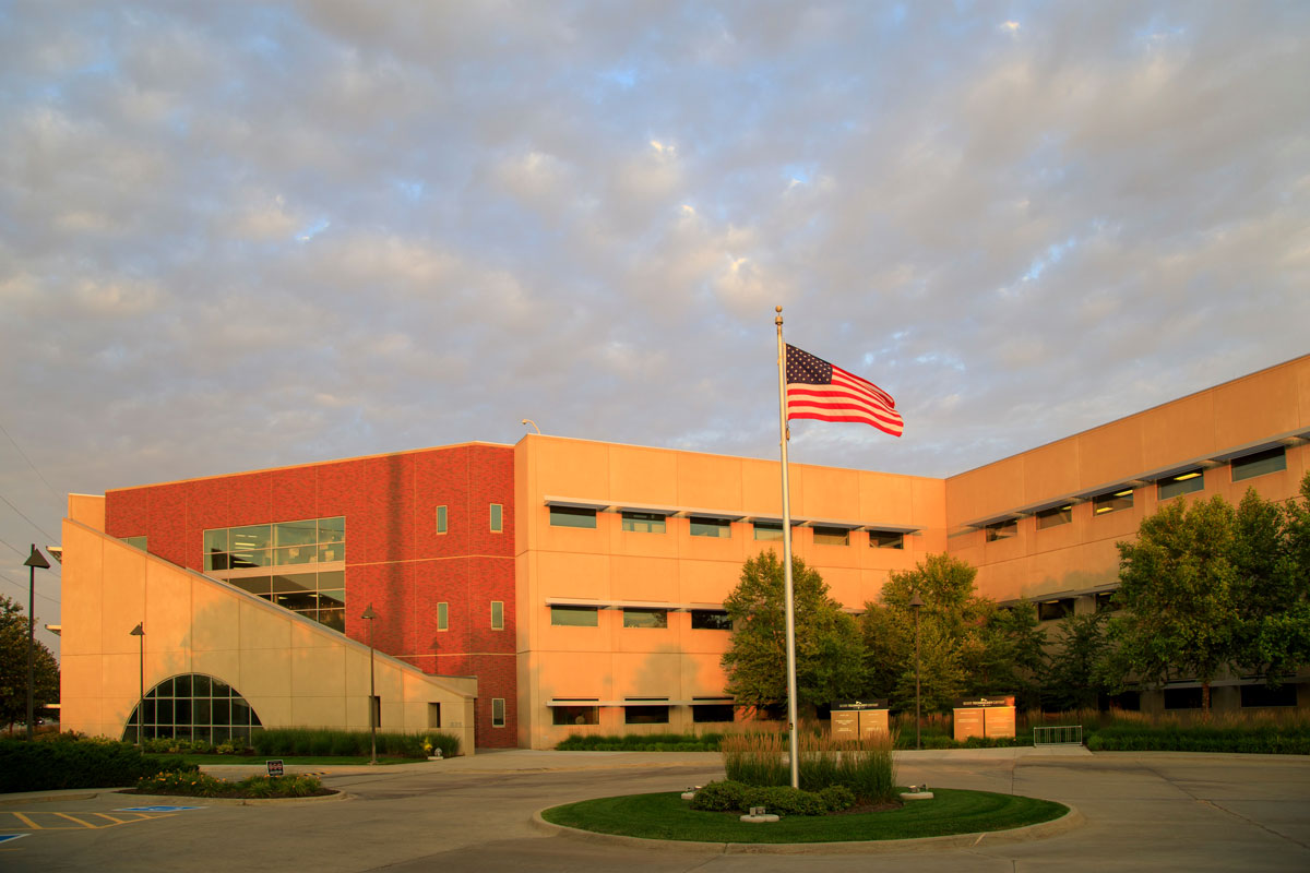 An image of the front door of the Scott Technology Center at sunset. The American flag flies on a flagpole in the center of a circle drive.