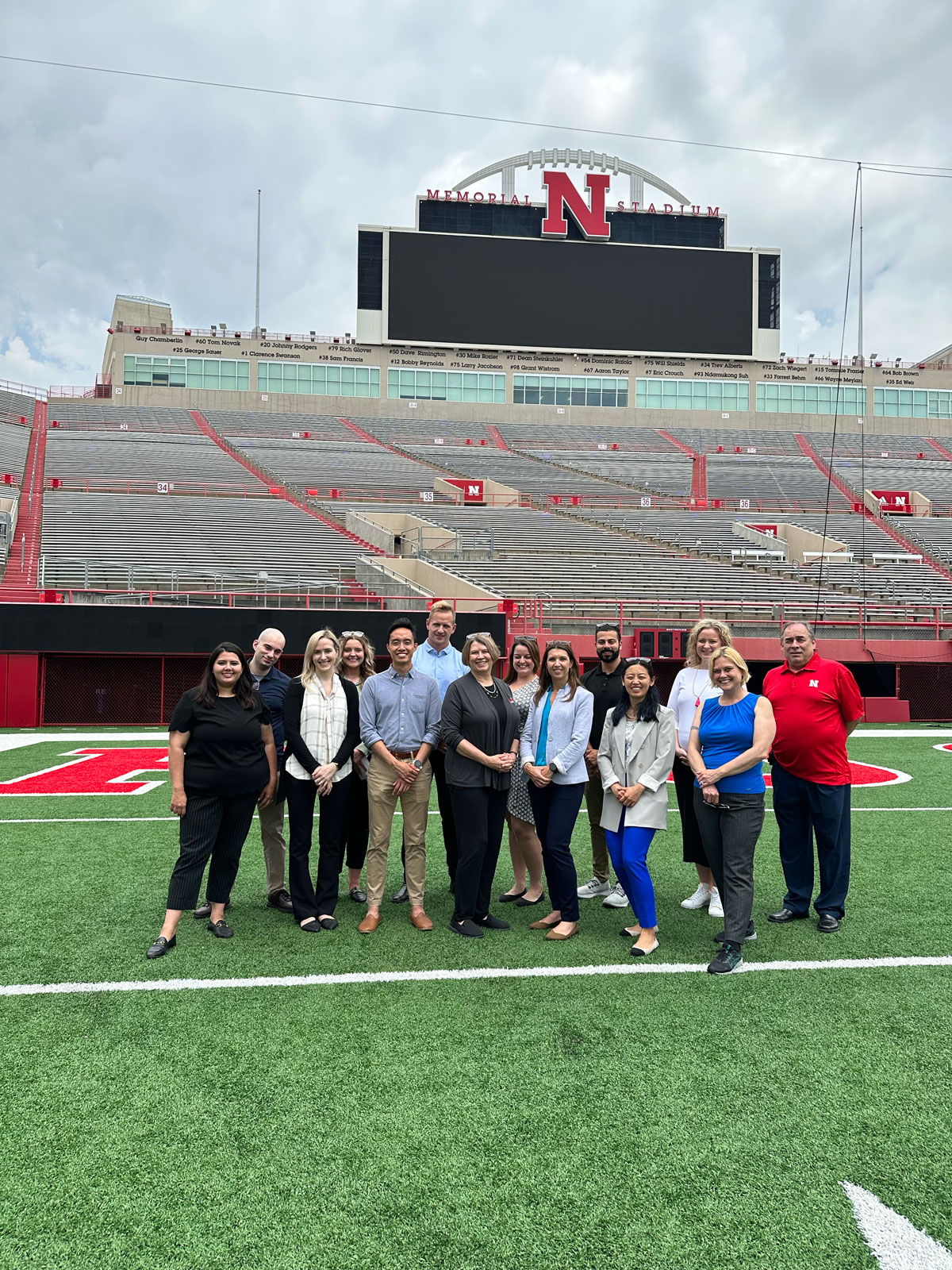 A group of 14 people pose for a photo in the end zone of Memorial Stadium. 