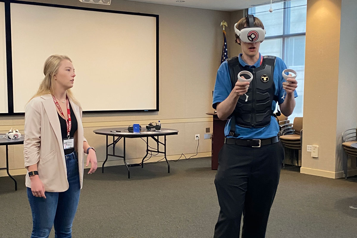 Madison Scott supervises a man with virtual reality goggles on.