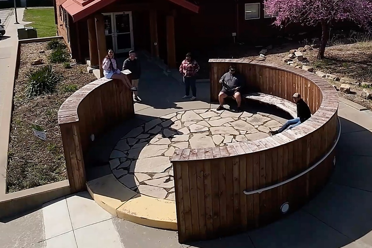 A drone shot of a group of students sitting in a circular wooden enclosure. 