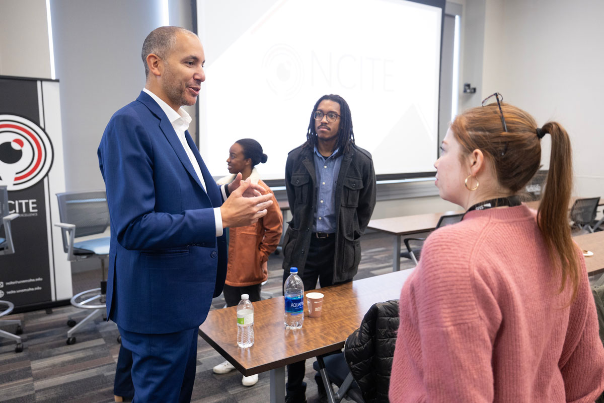 Dexter Ingram, wearing a blue suit, speaks with an audience member wearing a pink sweater following the panel discussion in January. NCITE's Anthony Roberson, wearing a dark gray jacket, looks on. 