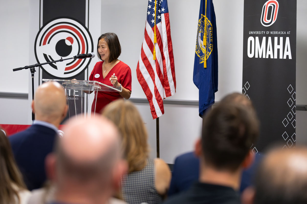 UNO Chancellor Joanne Li addresses the audience from a podium. Behind her are an American flag and the flag of the State of Nebraska. 