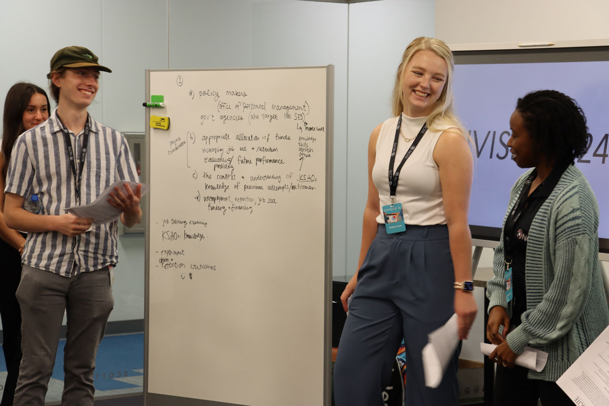 A shot of three smiling early career researchers standing aside a dry erase board. 