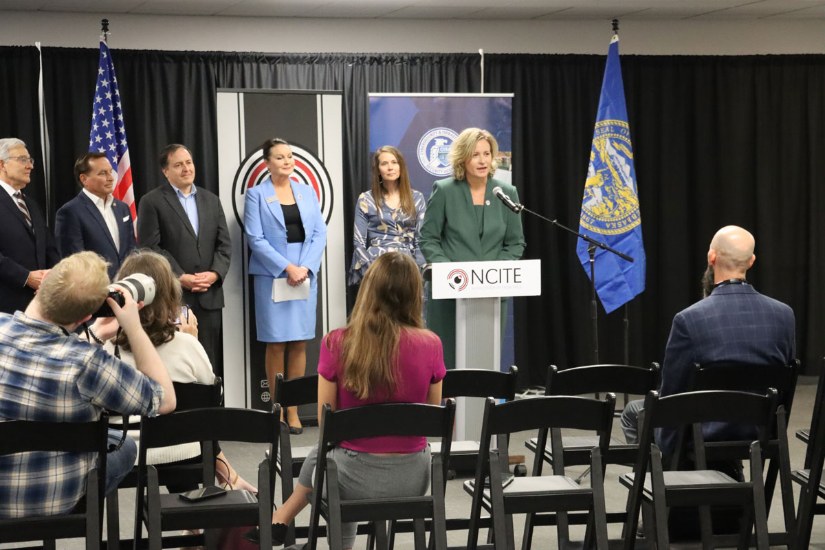 Gina Ligon stands at a podium bearing the NCITE logo. Behind her stands CISA Director Jen Easterly and four secretaries of state. 