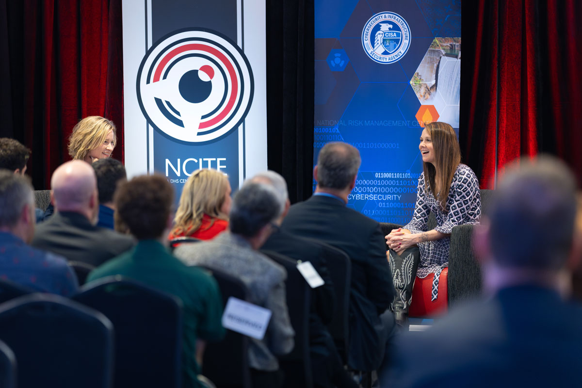 NCITE Director Gina Ligon and CISA Director Jen Easterly sit on a stage smiling before an audience.