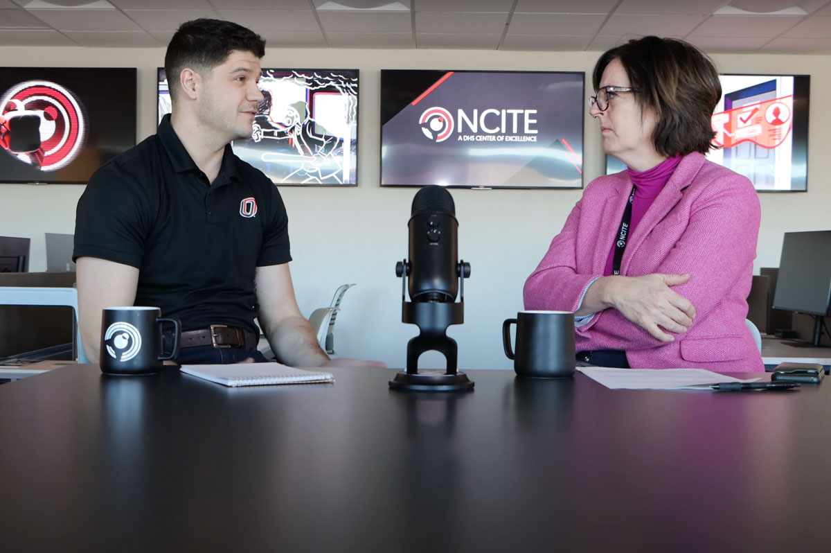 NCITE's Austin Doctor and Erin Grace sit at a table before monitors displaying NCITE branding. A microphone is set on the table between them. 