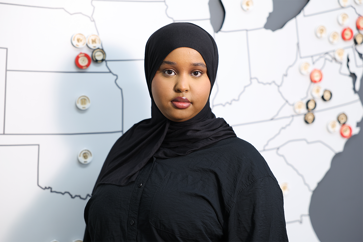 Headshot of recent UNO graduate Hafso Ibrahim standing in front of a map of the US with pinpoints on it.