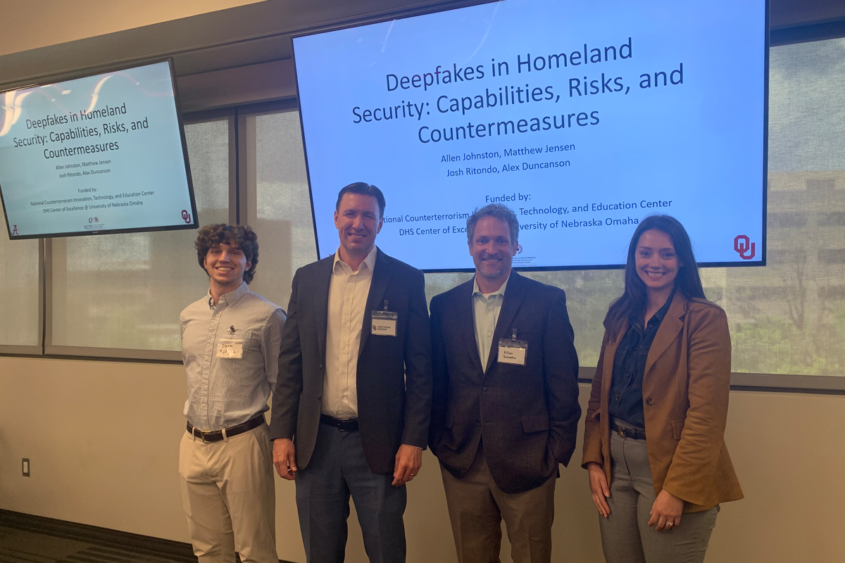Four researchers stand in front of presentation screens displaying a project titled “Deepfakes in Homeland Security: Capabilities, Risks, and Countermeasures.” The group poses for a photo in a conference or academic presentation space, with the research title and funding information visible on the screens behind them.