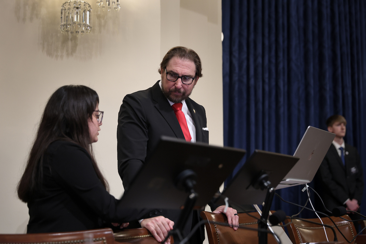 A congressional staff member speaks with an NCITE student during an artificial intelligence demonstration on Capitol Hill. They stand beside a laptop and presentation monitors in a congressional hearing room while discussing the AI technology.