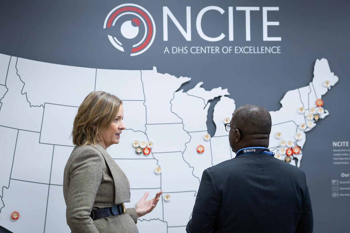 A woman gestures while speaking with a man in front of a large map highlighting NCITE's research partners across the United States at NCITE headquarters.